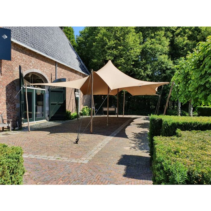een stretchtent van 6x10,5 meter zit met houten palen vast in de grond. Er staan twee palen in het midden om de gehele tent omhoog te houden. de houten palen zijn vastgezet met touwen en haringen die in de grond zitten.